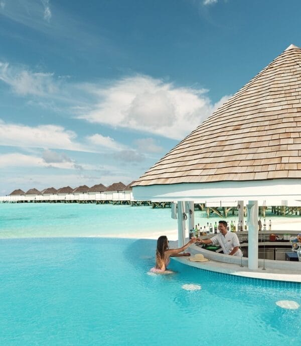 Guest relaxing in a pool getting a drink from a swim up bar at a tropical resort with overwater villas.