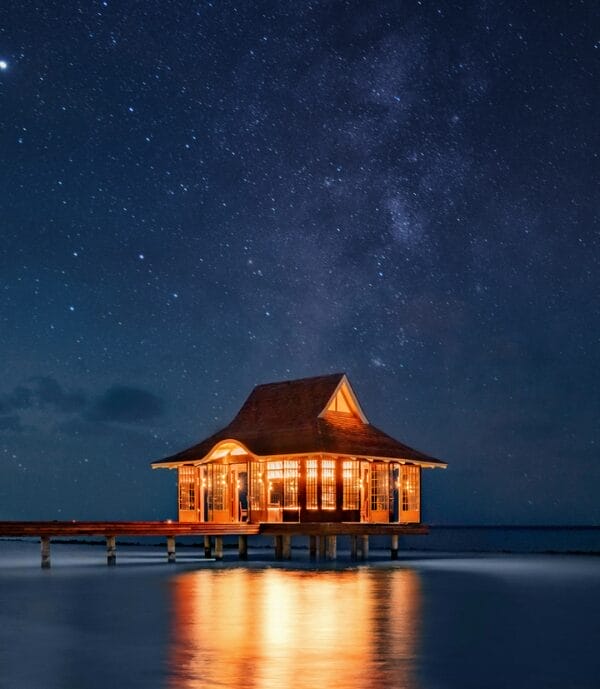 Overwater pavilion at night, illuminated against a starry sky.