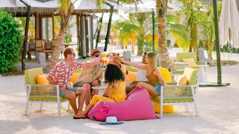 a young group of people sitting on chairs under palm trees with drinks at Wink