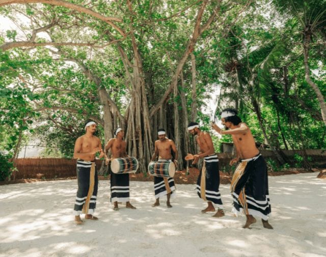 Five men wearing traditional Maldivian clothing, dancing and playing 'bodu beru', a Maldivian drum