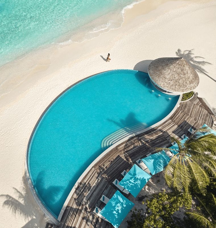 Aerial view of Solis Pool Bar over looking the ocean at Nova Maldives with a woman walking along the beach