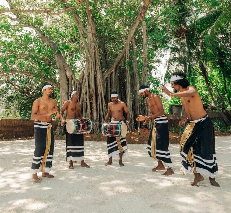 Five men wearing traditional Maldivian clothing, dancing and playing 'bodu beru', a Maldivian drum