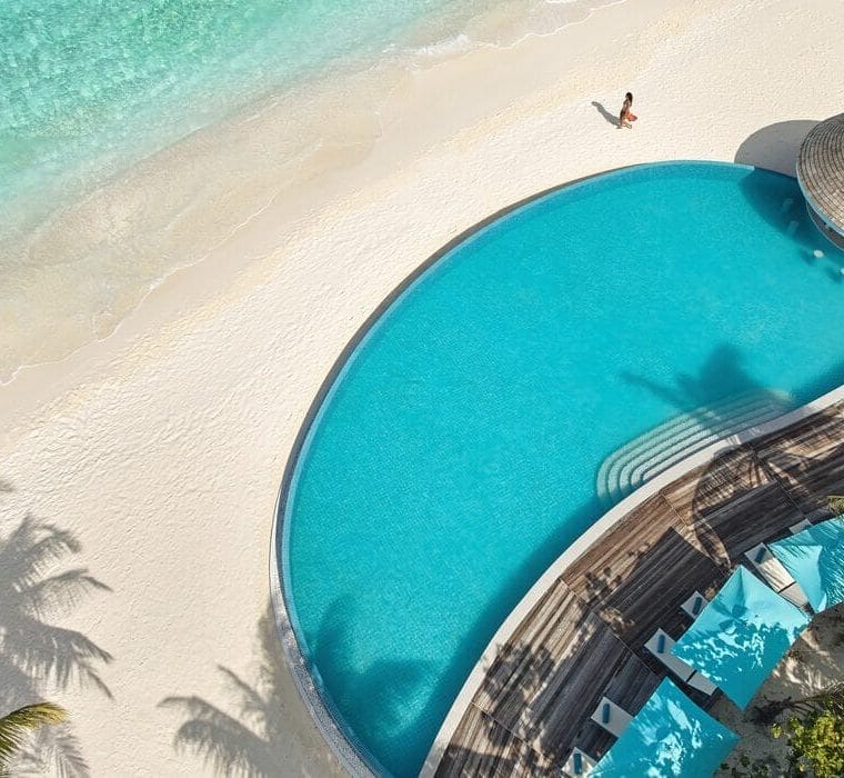 Aerial view of Solis Pool Bar over looking the ocean at Nova Maldives, with a woman walking on the beach
