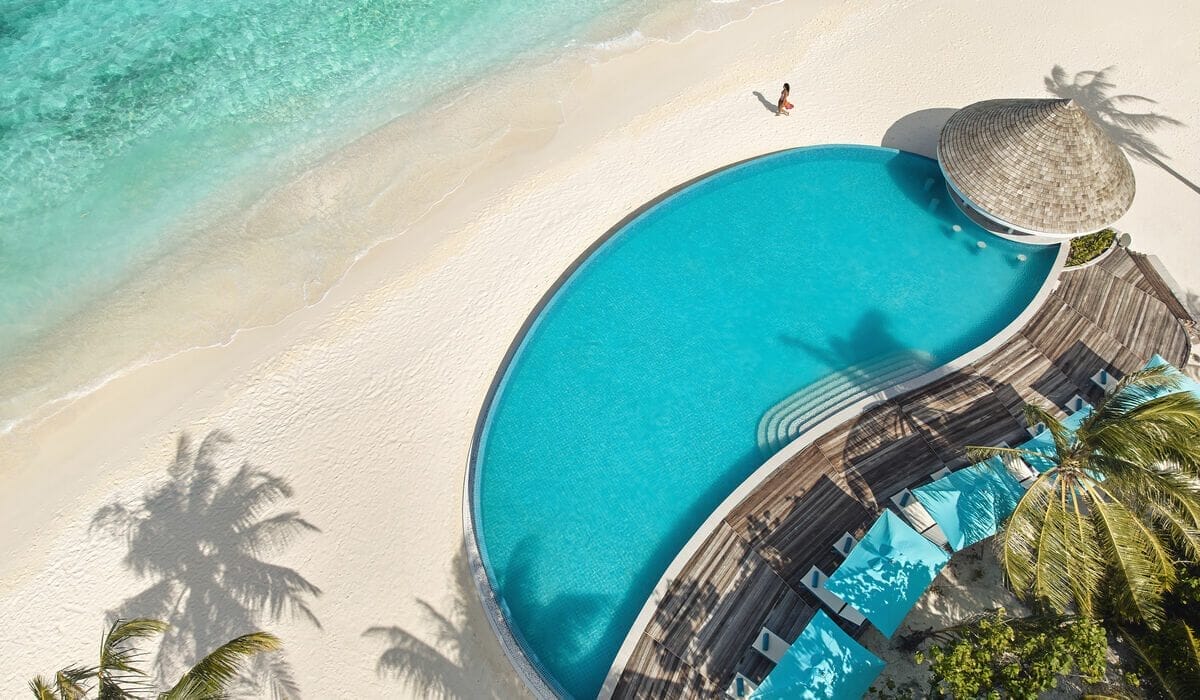 Aerial view of Solis Pool Bar over looking the ocean at Nova Maldives, with a woman walking on the beach