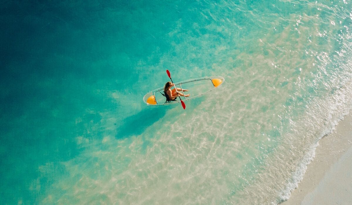 A woman rowing a glass-bottom kayak on the blue lagoon of Nova Maldives on a sunny day