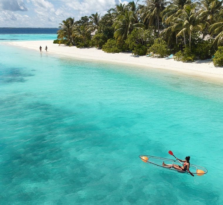 A person rowing a glass-bottom kayak away from the shore of Nova Maldives