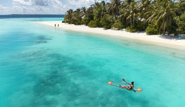 A person rowing a glass-bottom kayak away from the shore of Nova Maldives