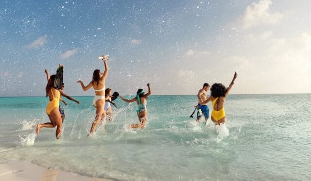 Group of friends running and jumping into the ocean, enjoying a beach day.