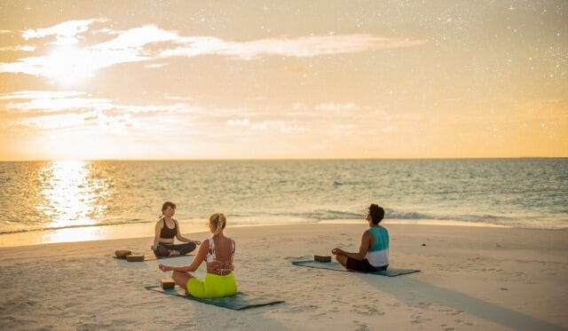 Group of people doing Yoga on the beach during sunset