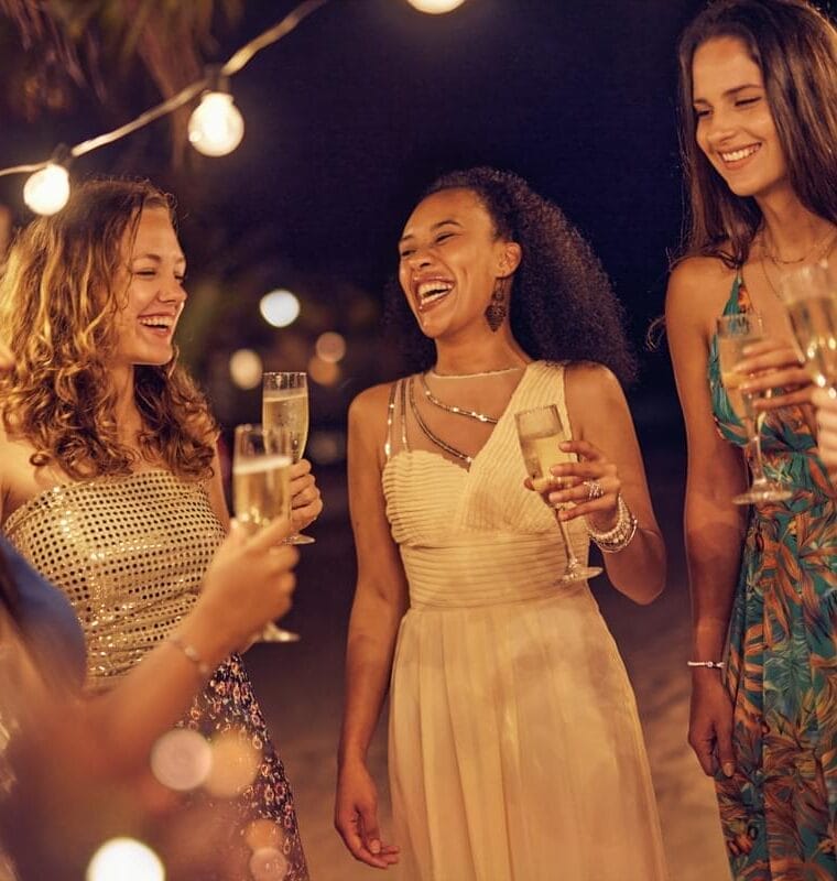 Group of women dressed in evening gowns, celebrating with drinks.