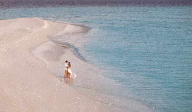 Couple walking along a sandbank stretching into the ocean.