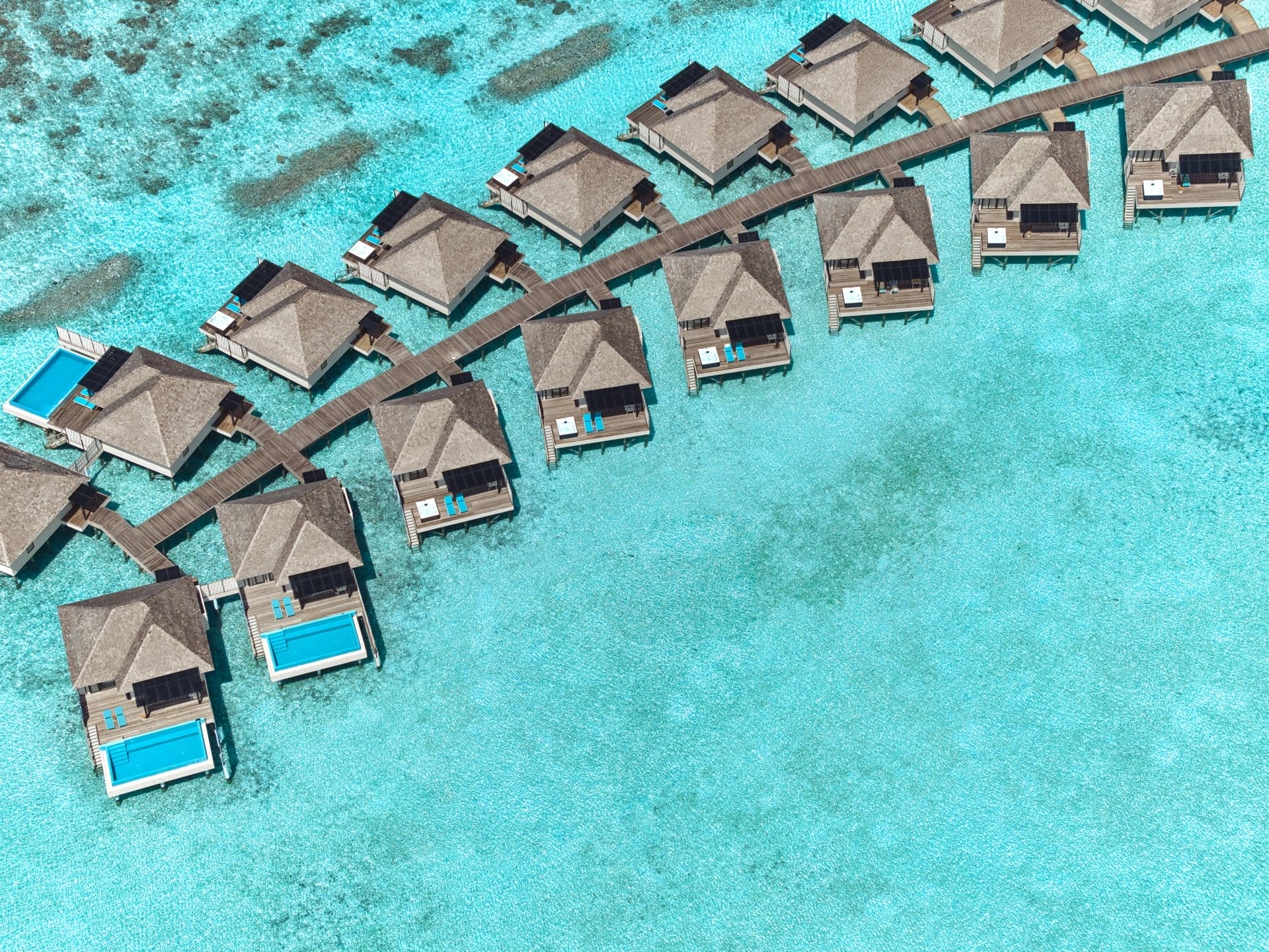 Aerial view of overwater villas and turquoise lagoon at a tropical resort.