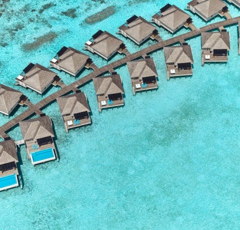 Aerial view of overwater villas and turquoise lagoon at a tropical resort.
