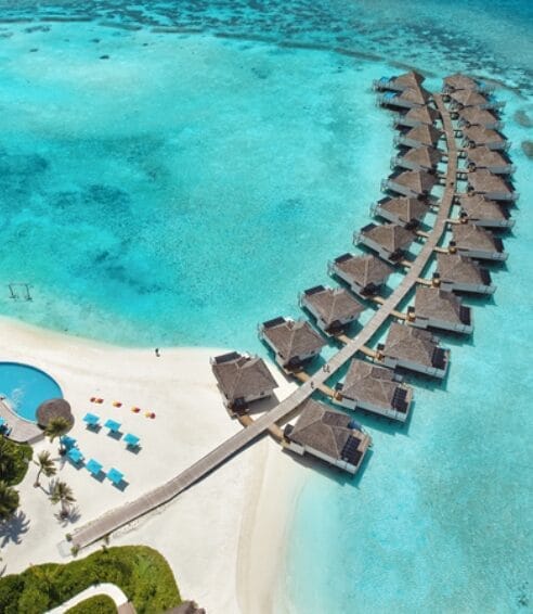 Aerial view of overwater villas arranged in a curve over clear turquoise waters.