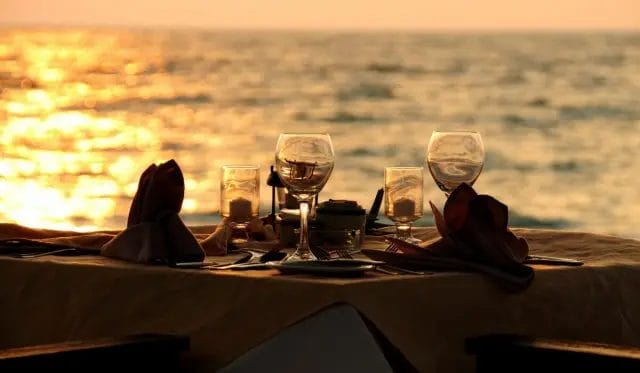 Elegant beachfront dinner setup with a romantic archway decorated with lights as the sun sets
