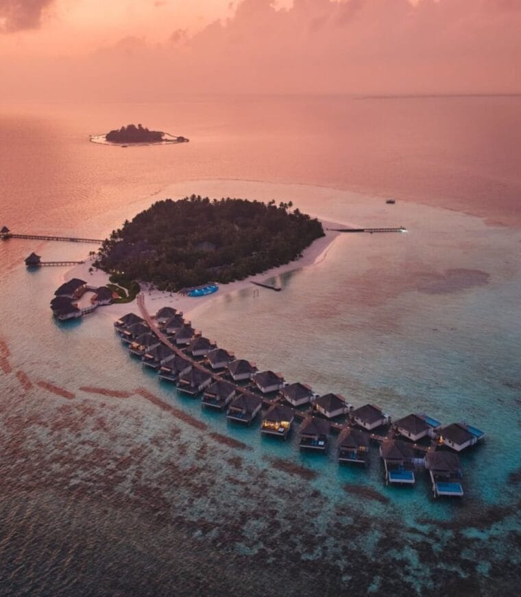 Aerial view of overwater villas at sunset with vibrant colors reflecting on the ocean.